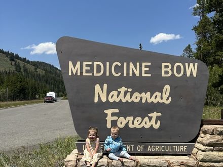 Two kids sitting on the Medicine Bow National Forest sign