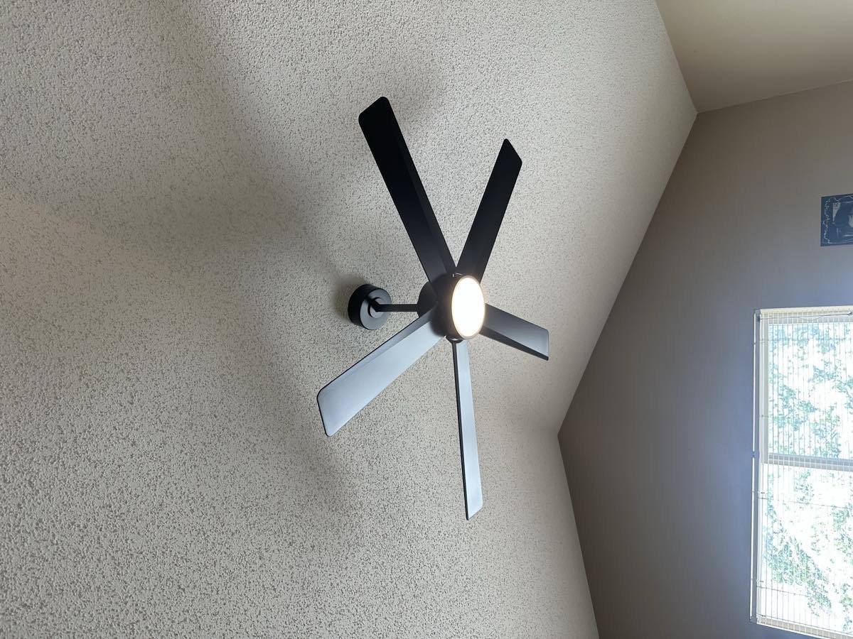 Black five-blade ceiling fan installed on a sloped ceiling with the light on