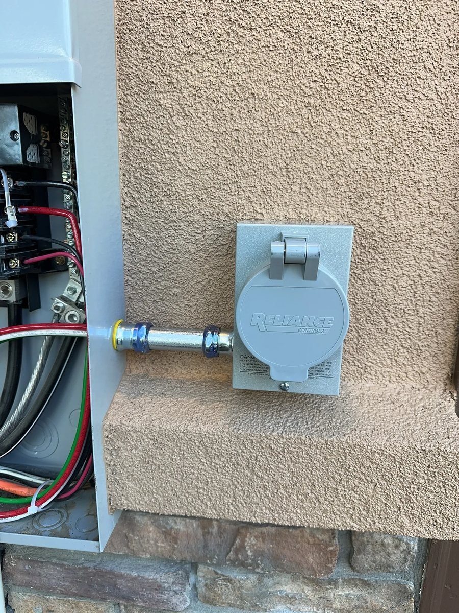 Weatherproof generator inlet on a stucco wall with the panel open beside it showing the wiring
