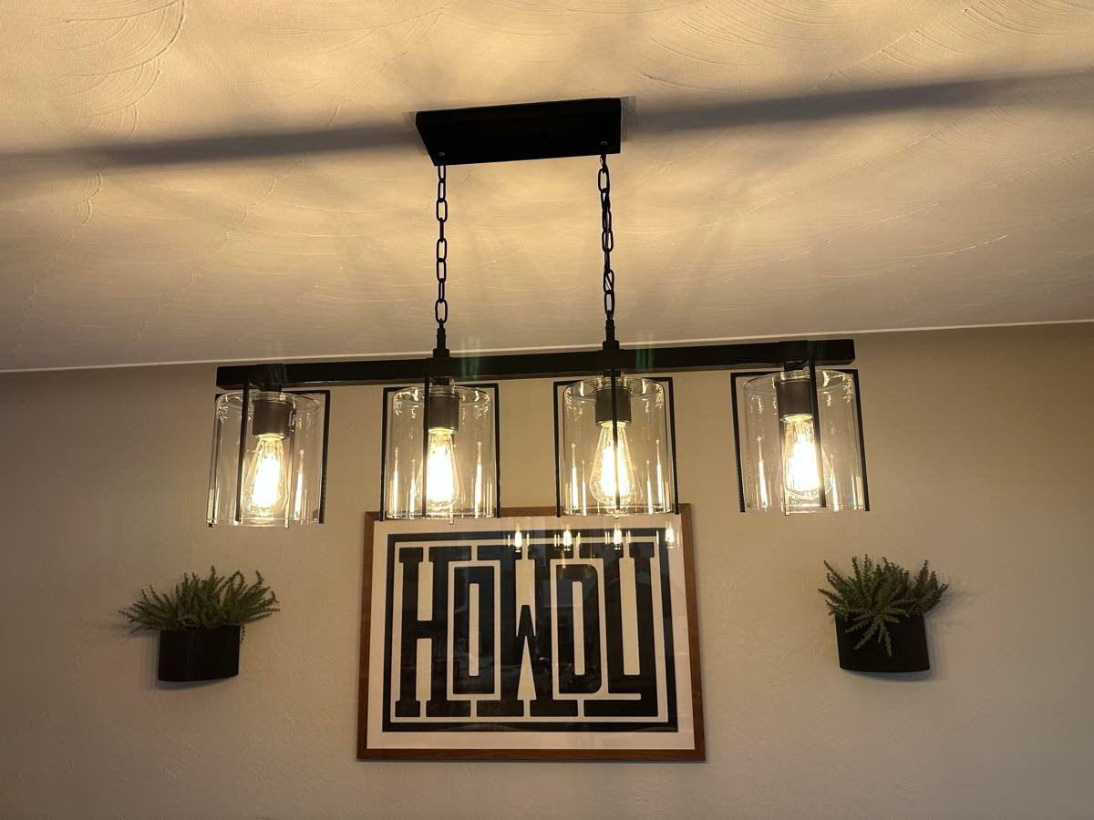 Black linear pendant light with four glass shades hanging over a dining area