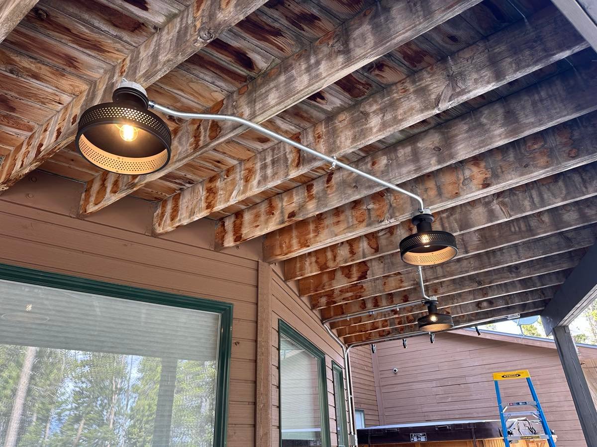 Three black barn-style pendant lights on exposed metal conduit under a wood beam patio ceiling