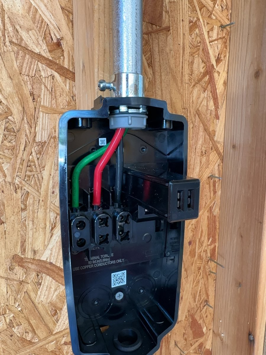 Tesla Wall Connector wiring compartment with the faceplate off, showing the conductors landed on the L1, L2 and ground terminals