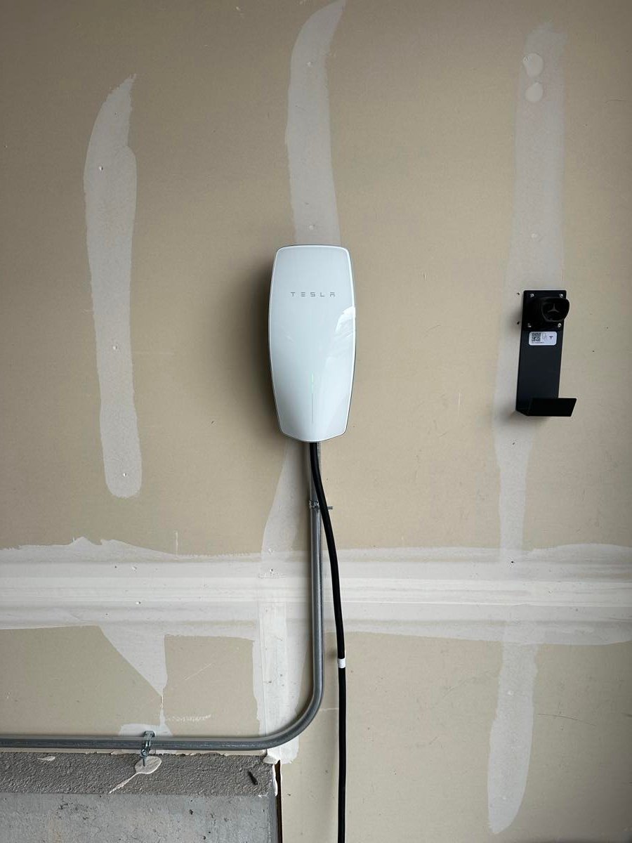 Tesla Wall Connector mounted on a garage wall with metal conduit running to it
